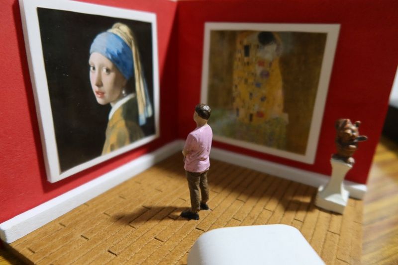 A close-up of a mini figure facing mini prints of Girl with a Pearl Earring by Johannes Vermeer and The Kiss by Gustav Klimt hung in a mini gallery diorama.