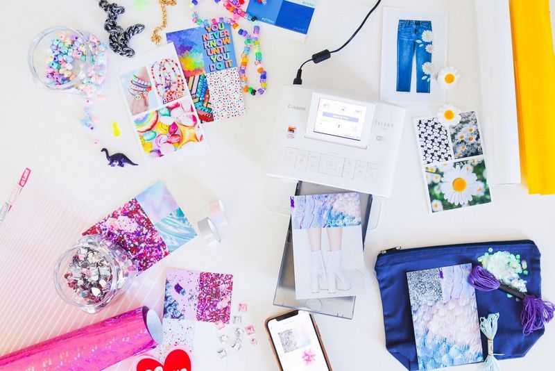An assortment of colourful crafting materials and prints around a Canon SELPHY CP1300 printer.
