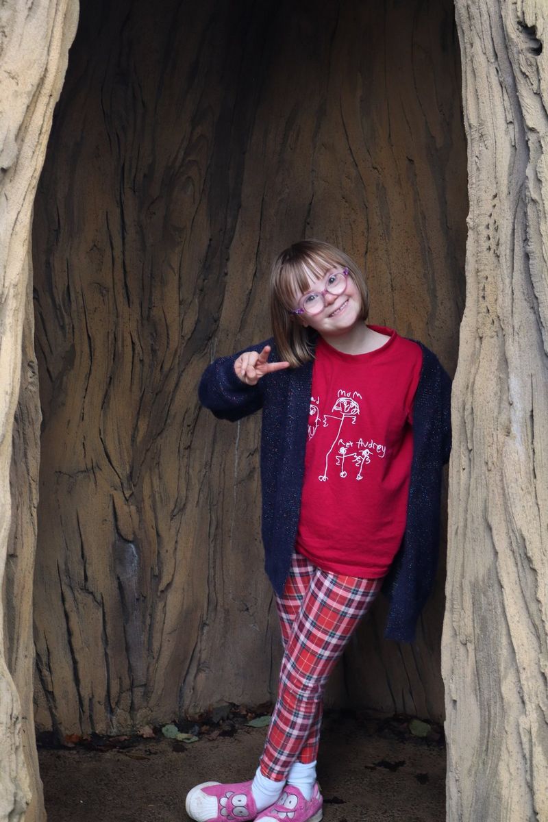 In a photo taken on a Canon EOS R100, a child stands framed in the opening of a hollow tree trunk.