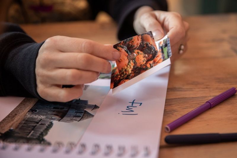 A pair of hands peels a photo sticker from its backing, ready to place it into an album.