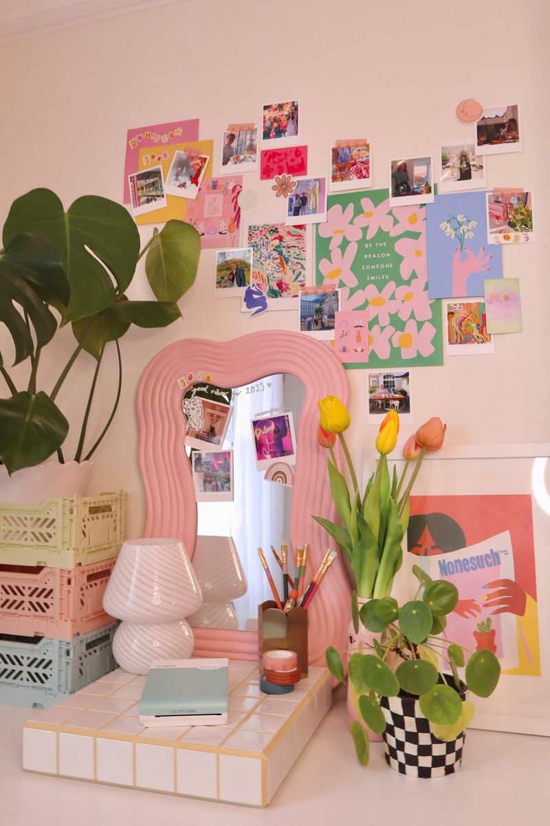 A green Canon SELPHY Square QX10 printer sits on a desk in front of a lamp and a mirror. The wall above is covered in colourful posters and prints.