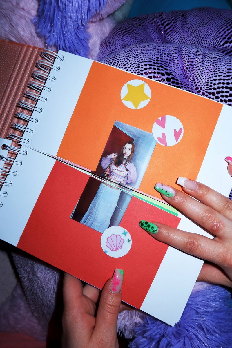 A pair of hands with brightly painted nails holds open a fashion lookbook with outfits cut in half to enable the top and bottom to be turned independently. 