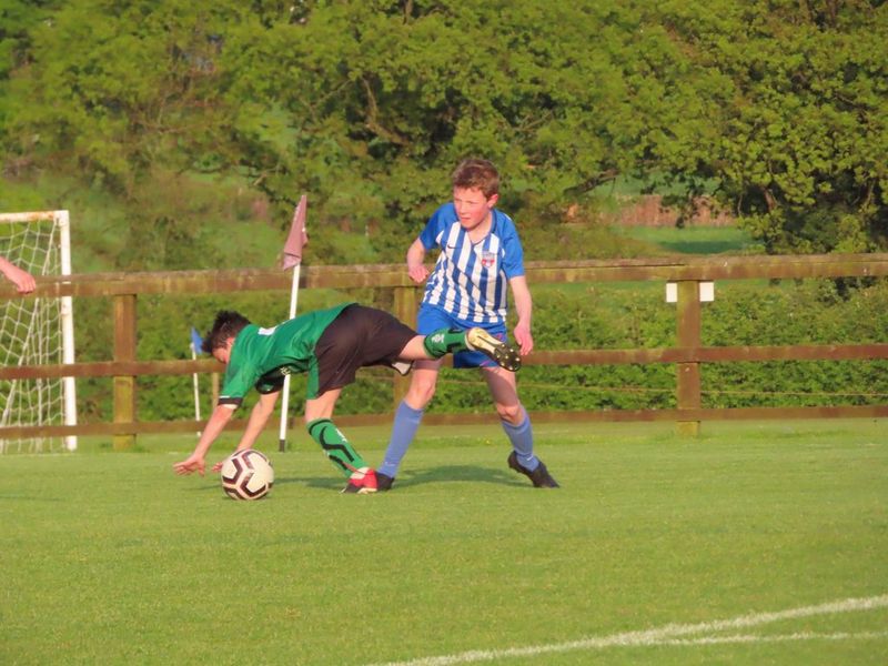Two boys in a football match, one trying to get the ball past the goalie, who is in position to intercept.