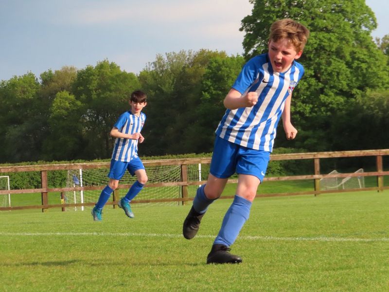 A boy on a football pitch, running while shouting happily in celebration.