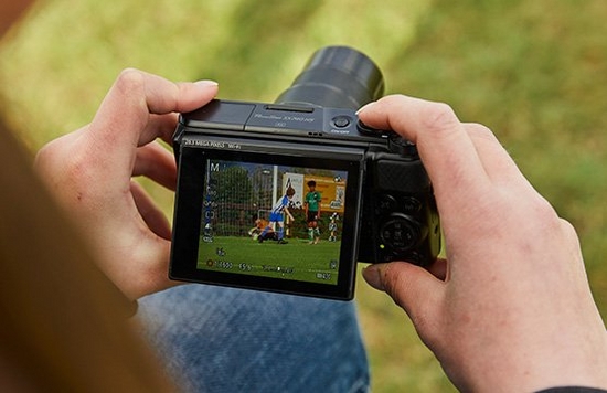 A person holding a Canon PowerShot SX740 HS looking at their shot on the flip up screen.