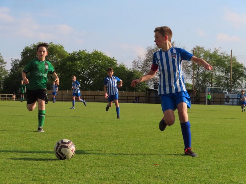 Boys playing football, one dribbling the ball while a player from the opposing team chases him.