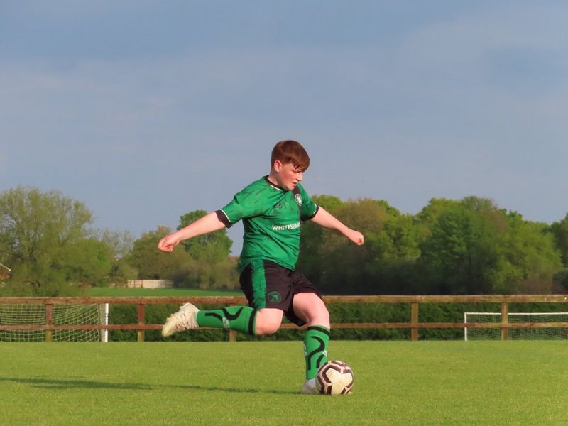 A boy about to kick the ball in mid-stride in a football match.