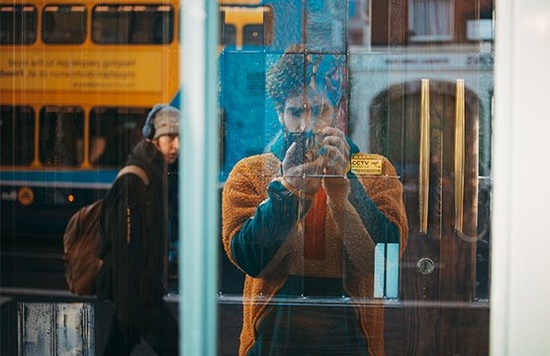 Giuseppe taking a photo of a shop window, showing passers by in the reflection.