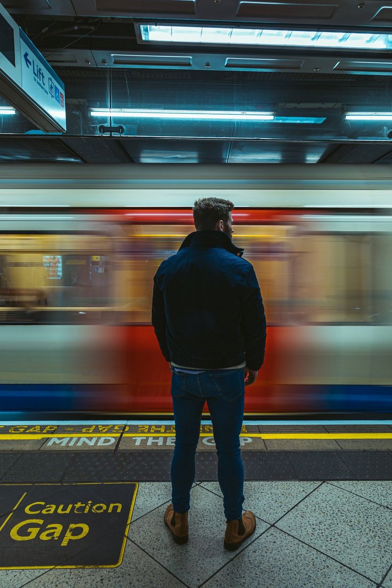 A person watches and waits on a platform as a train speeds past. The person is completely in focus while the train carriage is blurred.