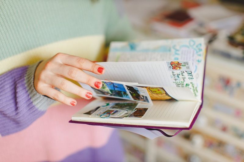 Hands hold and turn the pages of a travel journal, with colourful pictures and pieces clipped to the pages.