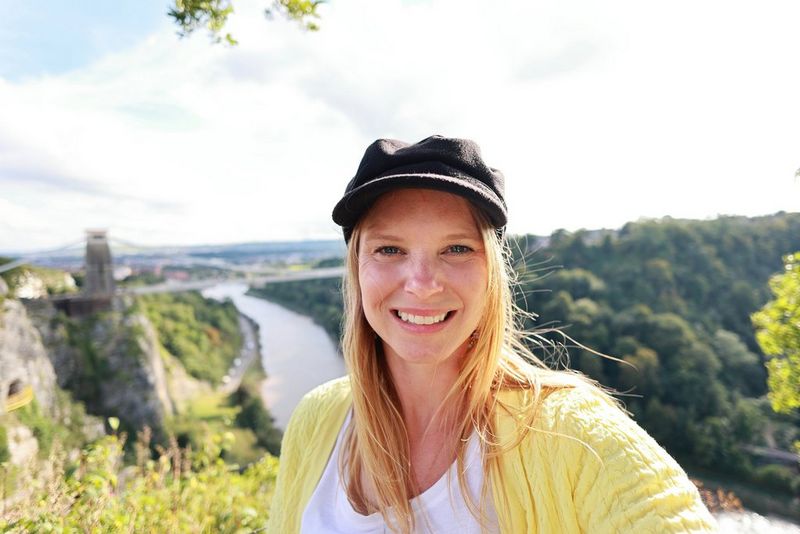  young woman standing in front of a wide view of a deep gorge spanned by a suspension bridge.
