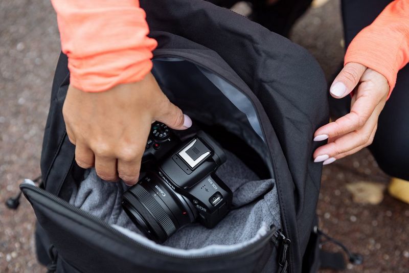 Hands placing a Canon EOS R50 into a black camera bag.