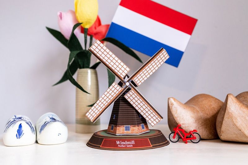 A papercraft windmill made from a Creative Park template displayed alongside a flag of the Netherlands, a small bike and a pair of wooden clogs.
