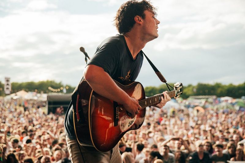 A rock musician on stage at a festival plays the guitar. Photo by Ben Morse.