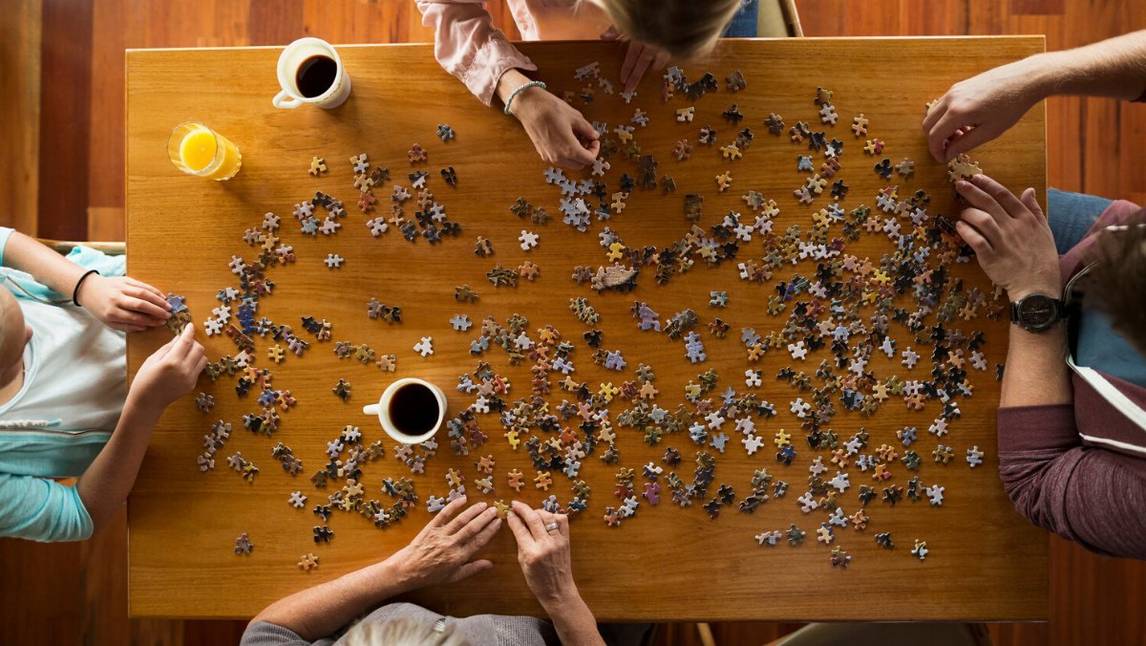 Group of friends completing puzzle on a table with coffee