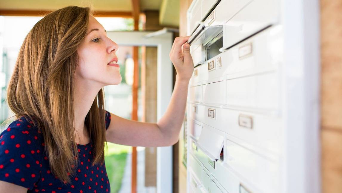Woman looking into postbox in shared mail area