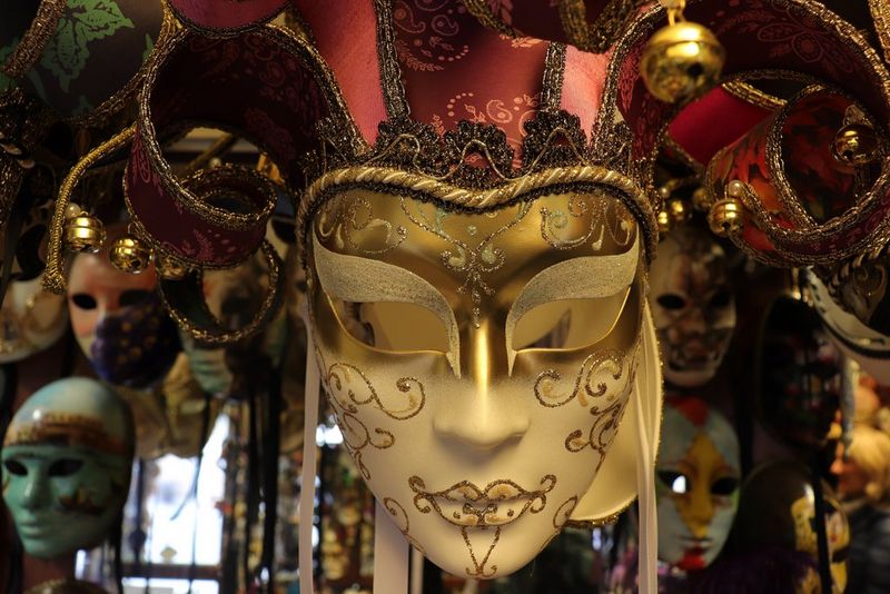 In a shot with a warm colour cast, a white carnival mask with gold patterning and scarlet headdress appears cream-coloured but richly detailed.
