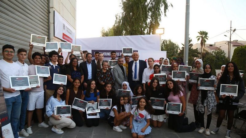 Around forty people, adults and young people, stand gathered in a group for a photo. A large number of the youngsters are proudly holding certificates. In the centre are several adults, dressed in office attire.