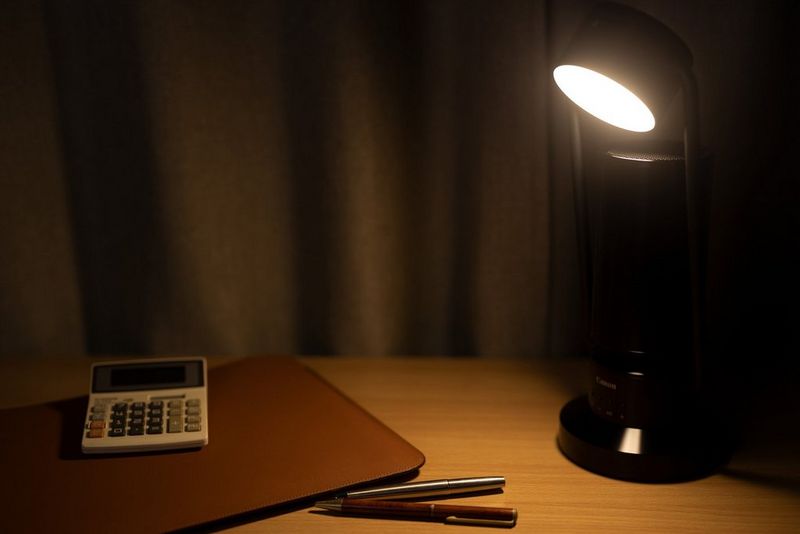A Canon Light & Speaker ML-A is positioned on a desk, shining a light onto a calculator and some pens.