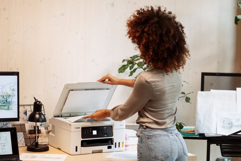 A person places a sheet of paper on the scanner of a Canon MAXIFY printer.