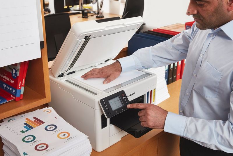 A man scans a sheet of paper on a Canon MAXIFY printer.