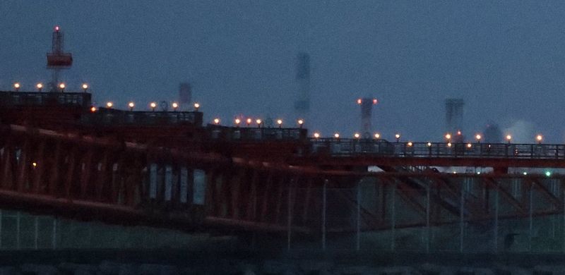  Detail from an image taken in low light at high ISO showing airport landing lights on elevated structures against a dark blue sky, with a lot of image grain and noise.