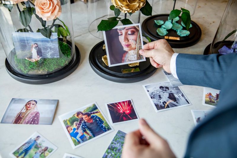 A user holds a photo print, with others spread on the table in front along with floral presentation displays.