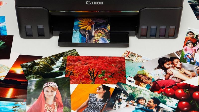 A Canon printer printing a colourful image, other images spread around the table in front of it.