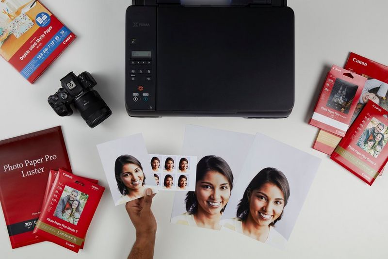 A top-down view of a PIXMA G650 printer surrounded by photo paper, printed photographs and a Canon camera.