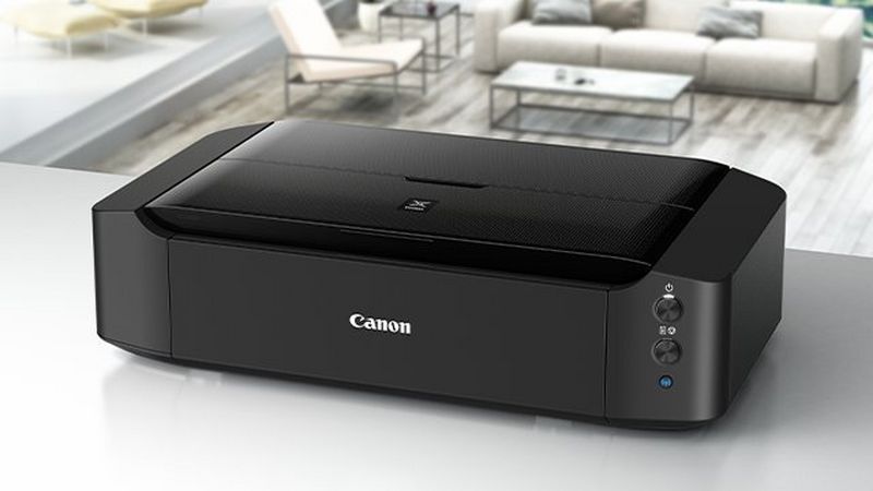 A black PIXMA printer on a white kitchen table with the living-room in the background.
