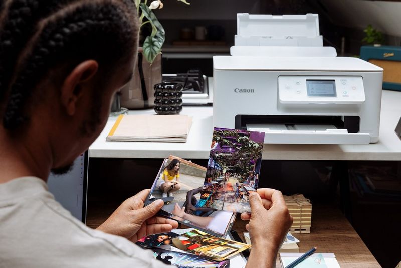 A person seated in front of a Canon PIXMA printer looking through a selection of photo prints