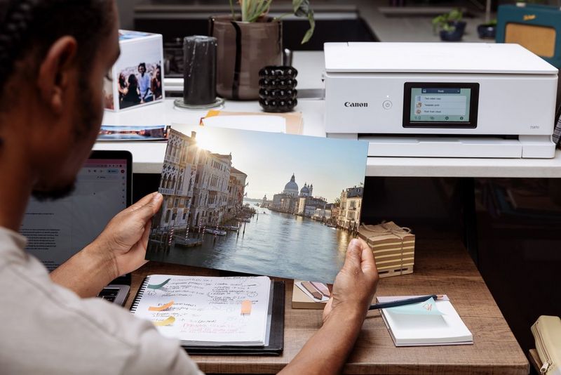 A man holds a print of a photo of the Grand Canal in Venice, with a Canon printer on a desk in the background.