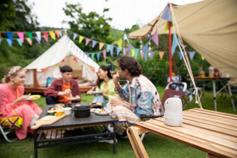 A Canon PowerShot PX positioned on a side table to capture four people eating food at a garden party.