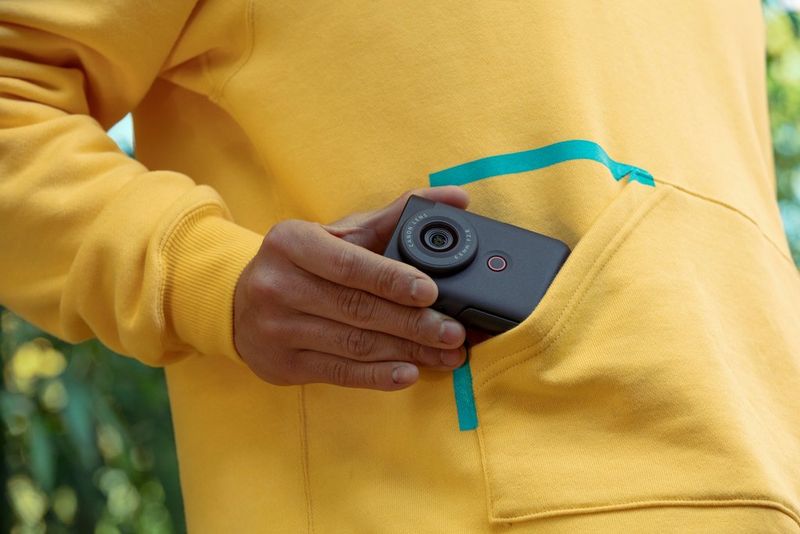 A user's hand draws a Canon PowerShot V10 from the pocket of a yellow long-sleeved sports top.