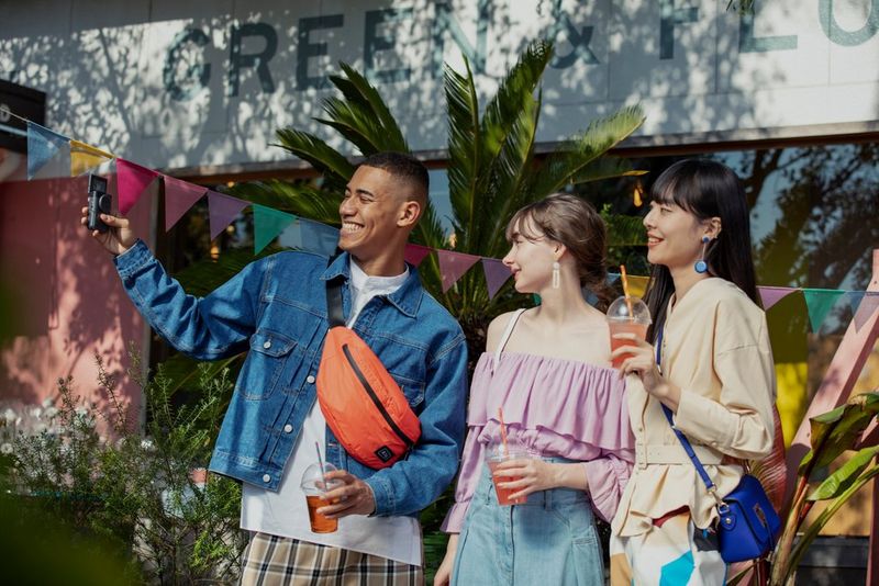 A group of people smile and pose while looking at a Canon PowerShot V10 held by the person on the left. 