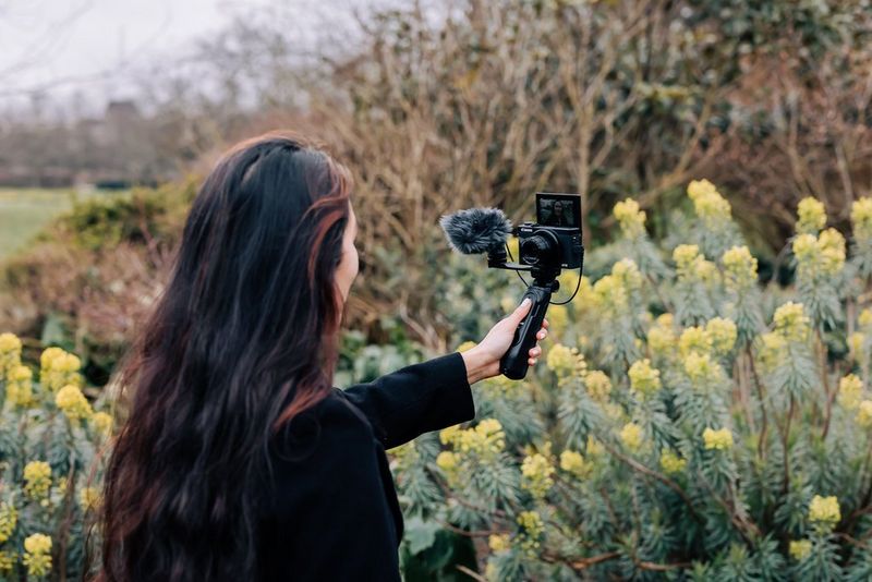 A woman in a garden films herself with a Canon PowerShot G7 X Mark III on a Canon Tripod Grip.
