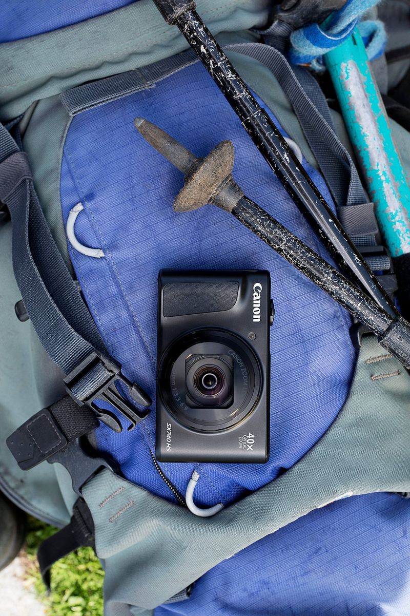 Shot from above, a Canon PowerShot SX740 HS camera on a blue backpack alongside walking poles.