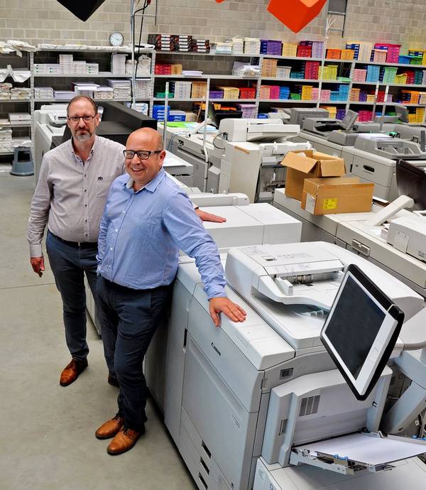 Two men stand next to a large printer