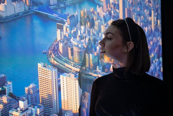 A side profile of a woman standing in front of an image of a city projected onto the wall.