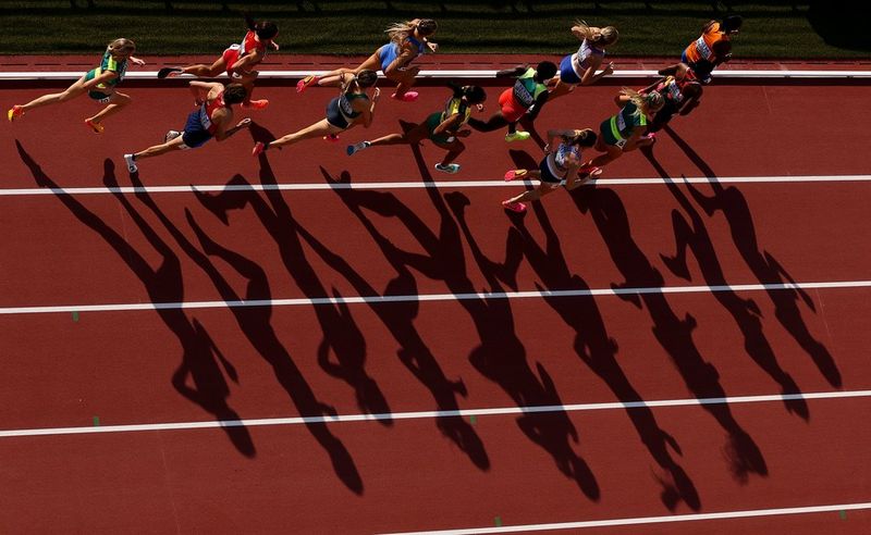Sprinters run along an athletics track, their shadows stretching out below them. Taken on a Canon EOS R3 with a Canon RF 100-300mm F2.8L IS USM lens.