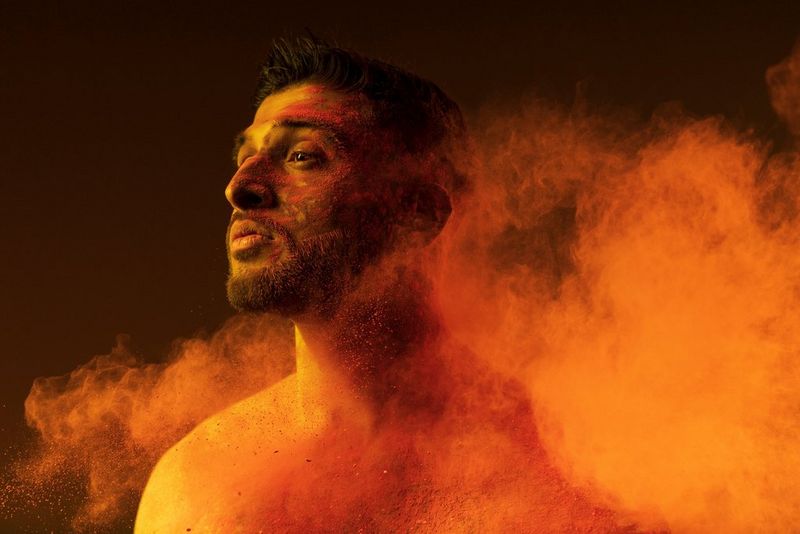 A person covered in red chalk and with plumes of chalk around him looks to the right in this portrait taken by James Musselwhite with a Canon RF 24-105mm F4L IS USM lens.