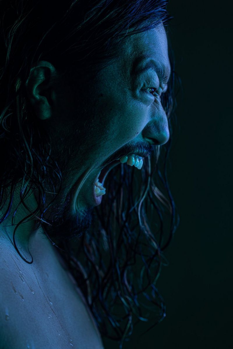 A side-on portrait of a person bathed in blue light and with his mouth open in a mock roar, taken by James Musselwhite with a Canon RF 100mm F2.8L MACRO IS USM lens.
