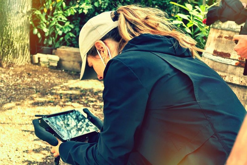 Director Basha de Bruijn, wearing a baseball cap and jacket, reviews footage on a monitor while seated on a film set.