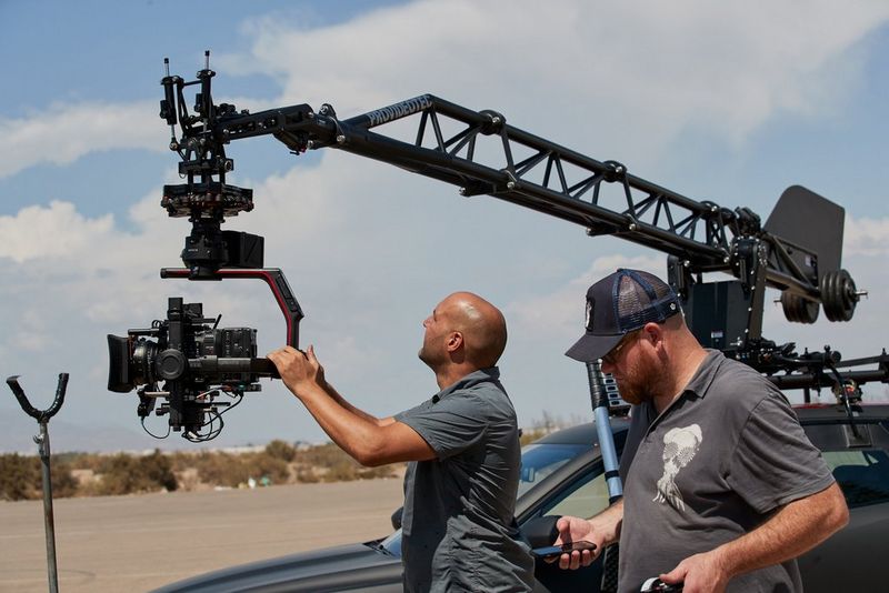 Technicians adjust a Canon EOS C500 Mark II with Sumire Prime lens in a Russian Arm attached to the roof rack of a motor car.