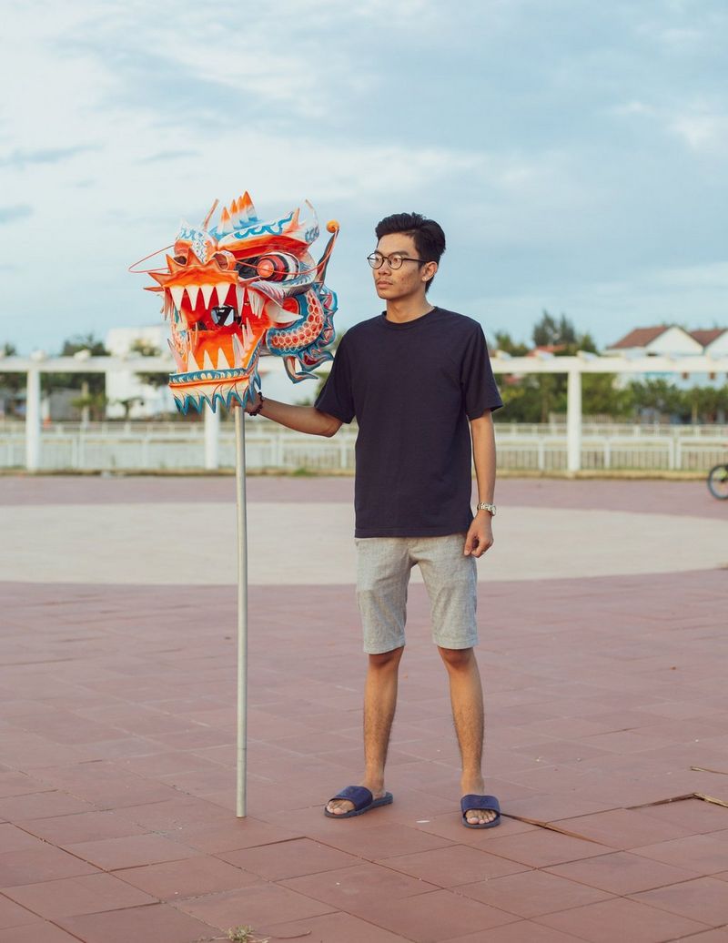 In a photograph by Travis Hodges, a man stands outdoors holding the head of a dragon on a stick.