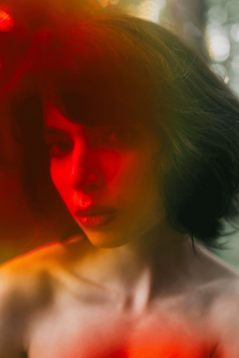 In an image by Sarah Köster, a close-up of a woman's face and naked shoulders are bathed in a red light.