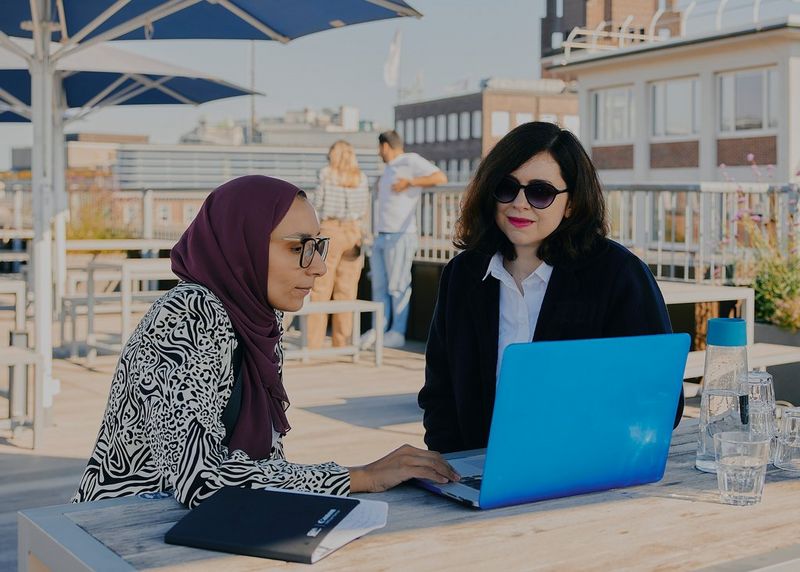 Seated in front of a laptop, Fatma Fahmy discusses her work with another woman during the Canon Student Development Program.