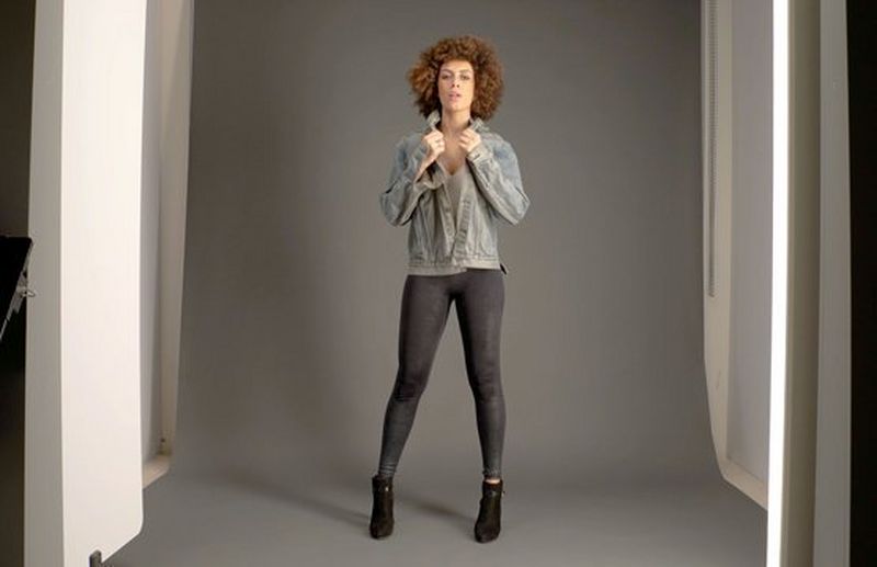 A fashion shoot for an online clothes company, with a woman wearing a denim jacket and black tights poses in a photography studio.