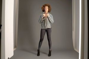 A fashion shoot for an online clothes company, with a woman wearing a denim jacket and black tights poses in a photography studio.