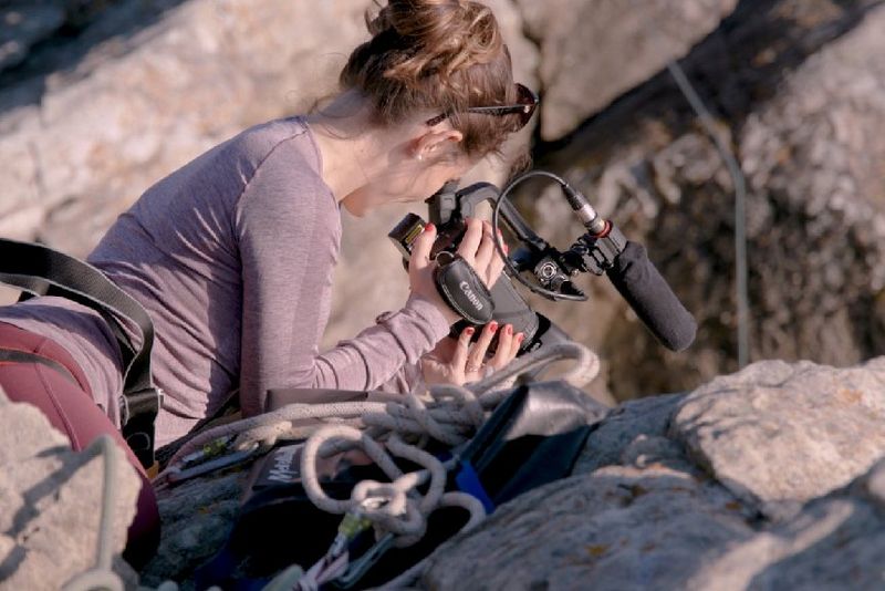 Journalist and cinematographer Elisa Iannacone lies on a ledge suspended from a rocky outcrop while filming with a Canon XA55 camcorder.